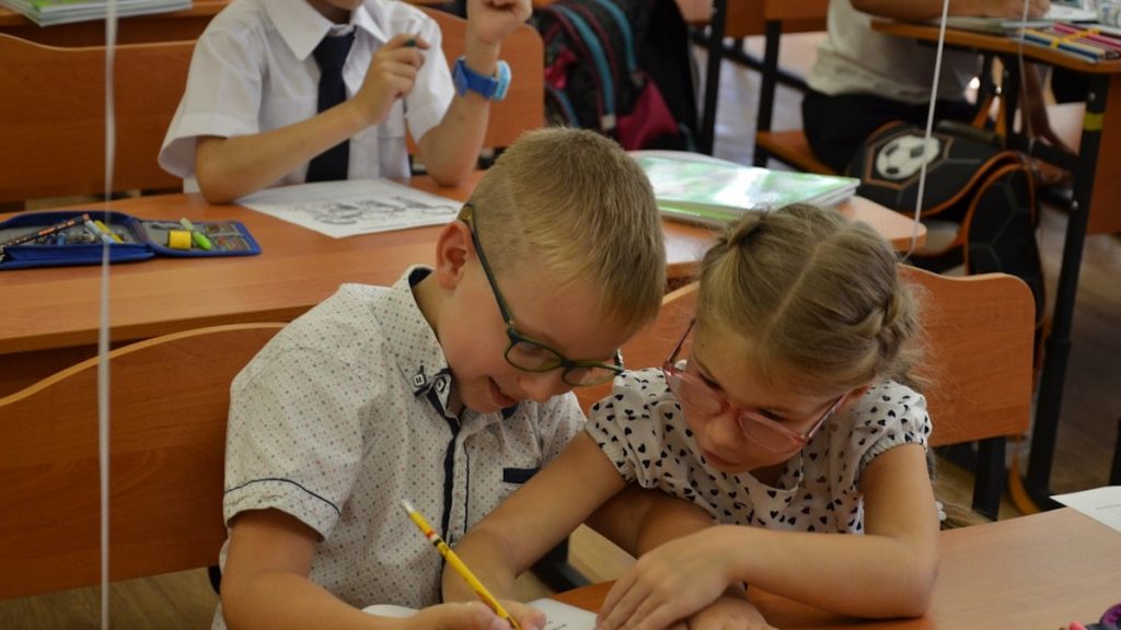 Two diverse elementary school children classmates studying together at desk